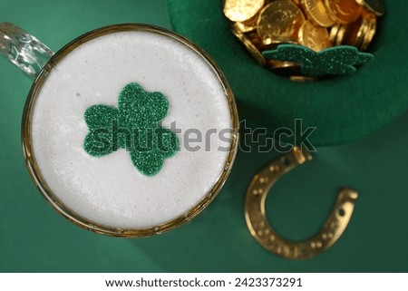 St. Patrick's day party. Green beer, leprechaun hat with gold, horseshoe and decorative clover leaves on green background, flat lay