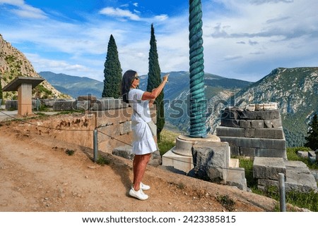 Journeys into Greek history:  A long-haired woman, wearing white dress  taking pictures of the Apollo Temple columns and ruins, illuminated by sunset. Delphi, Greece.