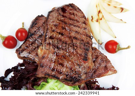 meat food : two roast steak boneless with red and chili peppers, served on green lettuce salad on dish isolated over white background