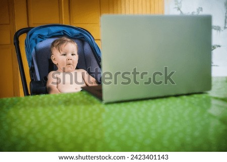 Happy baby boy sitting and watching cartoons on modern wireless computer laptop. The child smiles in a cheerful mood
