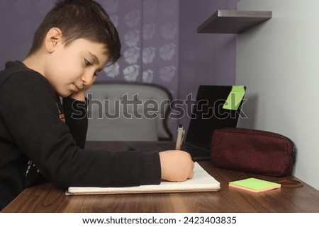 Distance learning online education. A schoolboy boy studies at home and does school homework. Bored student trying to write a composition. Stay at home concept idea.  Royalty-Free Stock Photo #2423403835