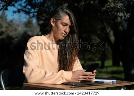 Woman teleworking with her cell phone in the garden of her house