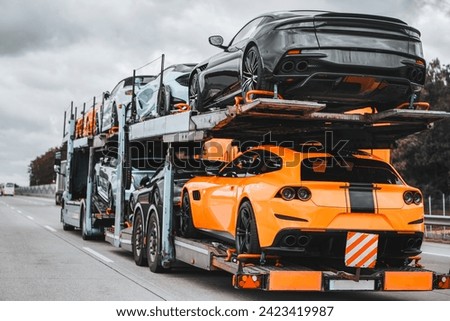 On a two-level hydraulic trailer truck, a load of exotic luxury sport cars gleams with speed and prestige. The ultimate supercars for racing or for showing off are delivered by a transport service.