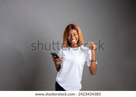 excited young lady holding her phone in an isolated grey background