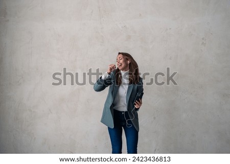 Charming woman and earphones on mobile to dance, stream music and podcast on gray background. Ecstatic adult female singing listening to playlist or audio, radio and studio mockup.