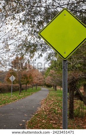 Fluorescent green triangular yield sign near a country walking path near trees