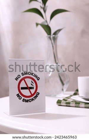 No Smoking sign and cup of coffee on white table indoors