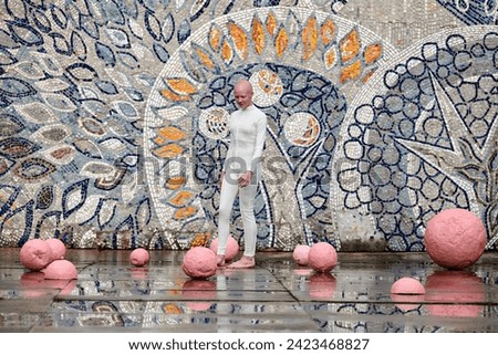 Young hairless girl ballerina with alopecia in white futuristic suit dancing outdoor among pink spheres on abstract mosaic Soviet background, symbolizes self expression and acceptance of unique beauty