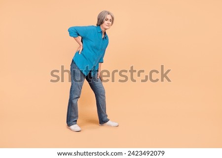 Full length photo of tired suffering pensioner person wear blue shirt jeans hold hand on lower back isolated on beige color background