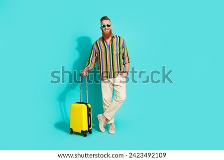 Full body length photo of handsome red hair casual tourist in trendy shirt waiting airport with baggage isolated on blue color background