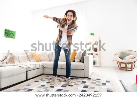 Full length photo of cheerful positive guy dressed checkered shirt listening music headphones dancing indoors house home room