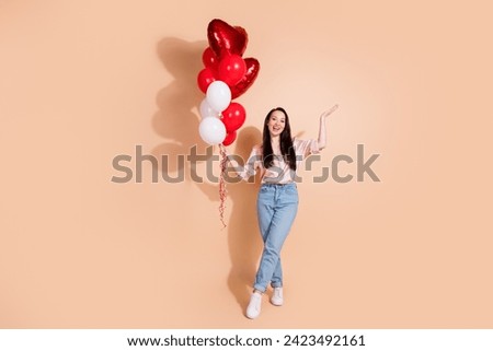 Full length photo of lovely girl wear pink shirt jeans pants hold balloons palm presenting empty space isolated on pastel color background