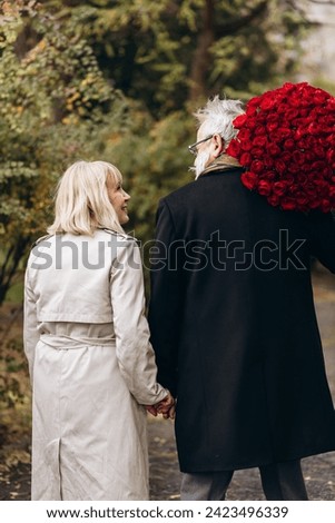 Elderly couple, handsome old man gives a huge bouquet of red flowers to his lady on a valentines day