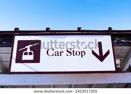 Stop car or Panoramic Ropeway. Wooden sign white with brown letters symbol Stop car arrow pointing down. Mounted on wooden beams under the station roof. parking spot. bright blue sky.