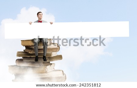 Young man with white blank banner sitting on pile of books
