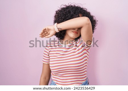 Young middle east woman standing over pink background covering eyes with arm, looking serious and sad. sightless, hiding and rejection concept  Royalty-Free Stock Photo #2423536429