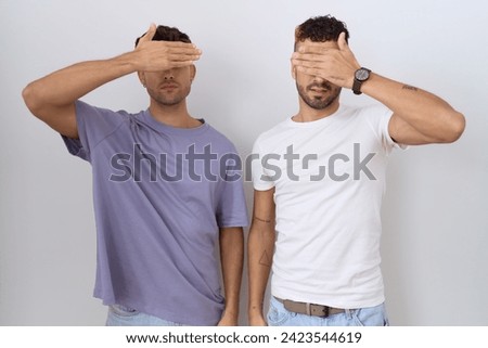 Homosexual gay couple standing over white background covering eyes with hand, looking serious and sad. sightless, hiding and rejection concept  Royalty-Free Stock Photo #2423544619