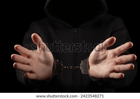 Unknown, indistinguishable thug or hucker in handcuffs and black clothes is arested. Concept: Crime. isolated on black background Royalty-Free Stock Photo #2423548271