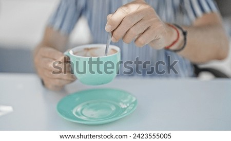 Close-up of a man stirring coffee in a turquoise cup at a modern cafe terrace.