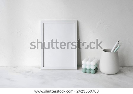 Empty poster mockup, green and white candle, pen on neutral marble gray table, empty textured concrete wall background, elegant minimal home interior still life, soft natural light.