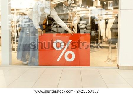 The seller in the store puts a banner with the action on the window. Season of discounts, sales. There is a sale in the clothing store. Black Friday.