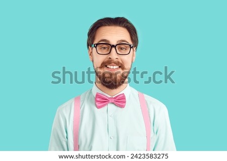 Portrait of funny male nerd hipster in stylish colored clothes on light blue background. Guy with mustache and beard in shirt, suspenders and glasses with funny expression looks at camera. 