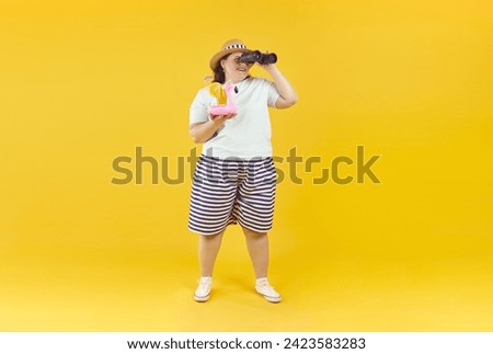 Funny chubby, overweight woman tourist looking through binoculars. Full length shot of plus size cheerful woman in summer clothes holding tropical cocktail on isolated studio background Royalty-Free Stock Photo #2423583283