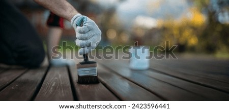 Close-up, a man's hand in a work glove with a painting brush paints boards outdoors. A hand applies paint, oil or varnish to the veranda floorboards