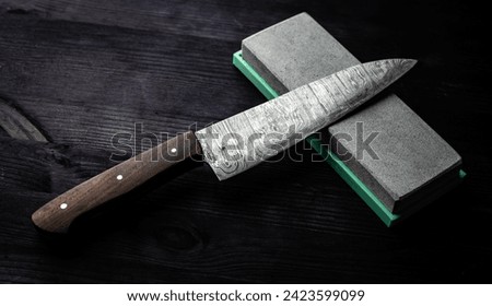 Sharp Chef's Kitchen Knife And Sharpening Stone Lie On Dark Table Royalty-Free Stock Photo #2423599099