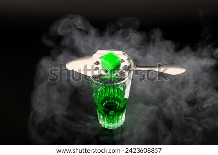 Green flavoured vodka called Absinthe served in a shot glass with a special spoon with white sugar cubes