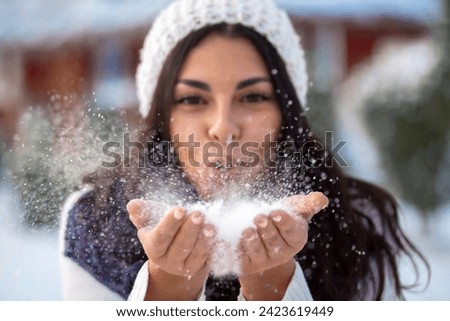 Winter. Woman with wearing ear muffs blowing on snow in hands, Girl in the park in winter blowing snowflakes	