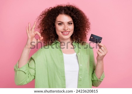 Photo portrait of attractive young woman hold credit card show okey symbol dressed stylish green clothes isolated on pink color background