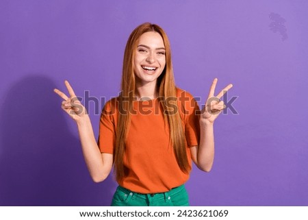 Portrait of happily red hair young lady wearing orange t shirt showing v sign good to see you here isolated on violet color background