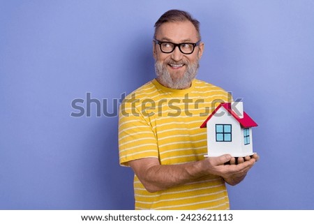 Photo of positive senior man dressed striped t-shirt in eyewear look at sale empty space hold house isolated on purple color background
