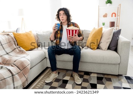 Full length photo of shocked funny guy dressed checkered shirt enjoying can cola pop corn watching intrigue movie indoors house home room