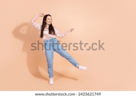Full length photo of cute girl wear pink shirt jeans pants stand on one leg look at promo empty space isolated on pastel color background