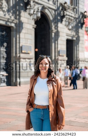 Happy young mexican woman in embroidered top looking at screen of smartphone while standing in front of blurred Munal museum in downtown Mexico City and browsing pictures in daylight