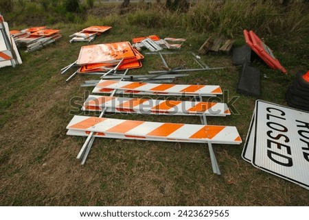 Close up of a white and black and black and orange Detour  Ahead signs on the grass . In a field in late afternoon. Barricardes and sidewalk closed sign behind. 

