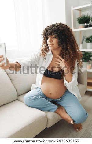 Pregnant woman blogger sits on the couch at home and takes pictures of herself on the phone, selfie and video call, consultation with the doctor online, pregnancy management