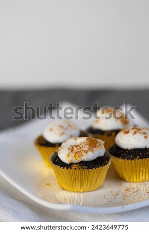 Chocolate cupcakes with white marshmallow icing, real edible gold leaf sprinkles in a gold cupcake wrapper on a white plate with room for text in the image - 4 cupcakes portrait