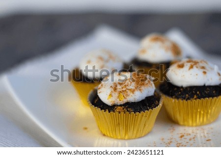 Chocolate cupcakes with white marshmallow icing, real edible gold leaf sprinkles in a gold cupcake wrapper on a white plate with room for text in the image - 4 cupcakes wide