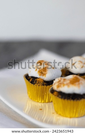 Chocolate cupcakes with white marshmallow icing, real edible gold leaf sprinkles in a gold cupcake wrapper on a white plate with room for text in the image - 3 cupcakes portrait