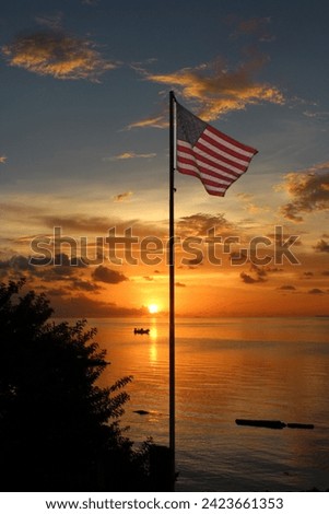 American flag on flagpole waving in the breeze at sunset with orange skies, reflected over the bay in Florida