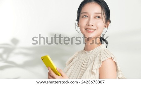 A young Asian woman holding a smartphone and smiling.
