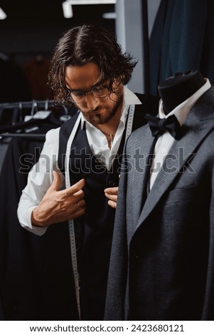 Handsome man tailor in glasses fitting bespoke suit to men in atelier. Concept dressmaker handmade couturier.