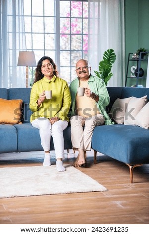 Portrait of senior Indian couple sitting on sofa or stairs and having coffee Royalty-Free Stock Photo #2423691235