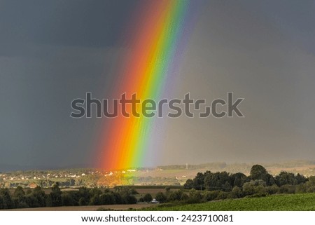 Landscape shot of a rainbow on the horizon over a landscape with houses and a gray, overcast sky Royalty-Free Stock Photo #2423710081