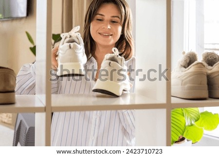 Woman arrangement sneakers on shoes closet shelf comfortable storage organizing method at home. Female footwear cupboard organize neatly folded boots seasonal wardrobe cleaning and maintaining Royalty-Free Stock Photo #2423710723
