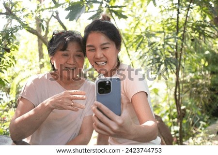 Asian Thai daughter and elder mother taking selfie together with happiness, while spending time together at cafe in garden on holidays. High quality photo