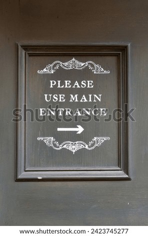 Framed Sign on Wall with Arrow on Wall of Building 'Please Use Main Entrance'